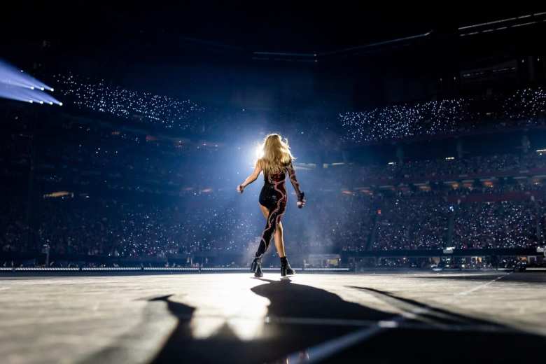 Taylor Swift de espaldas en el escenario con los asistentes en el fondo.